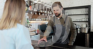 Happy man cafe owner entrepreneur making coffee for a customer in a cafe. Female customer pays for take away coffee with