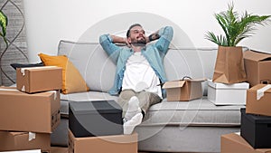 happy man with cardboard boxes in new home on moving day, relaxing on sofa relocation