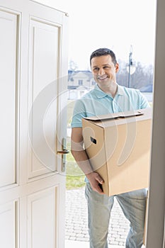 Happy man carrying cardboard box while entering new house