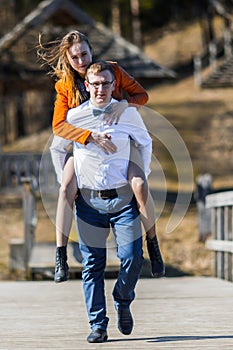 Happy man carrying his girlfriend on the back on on the bridge o