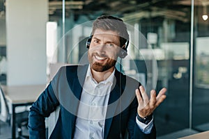 Happy man CEO having video call, using headset and talking at laptop webcamera, having video chat with business partners