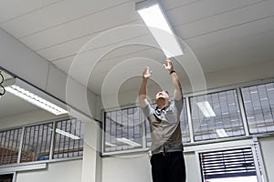 Happy man changing a light bulb at home. High angle shot energy-saving light bulb in a white lamp on the ceiling