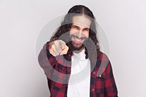 Happy man in checkered red shirt points at camera with index fingers, picks someone smiles broadly.