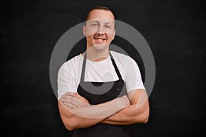 Happy man chef in apron looking at camera on black background.