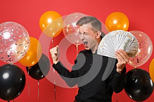 Happy man in classic shirt screaming clenching fist like winner holding bundle lots of dollars, cash money in hand on