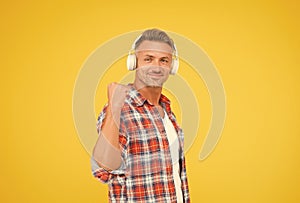 Happy man clench fist listening to music playing in modern earphones yellow background, audio