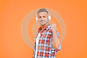 Happy man clench fist listening to music playing in modern earphones yellow background, audio