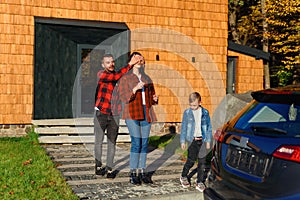 Happy man closes his wife`s eyes with his hands and leads her to a new black car. Present for woman.