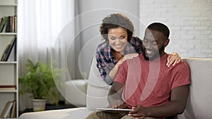 Happy man consulting with wife about buying new car, showing offers on tablet