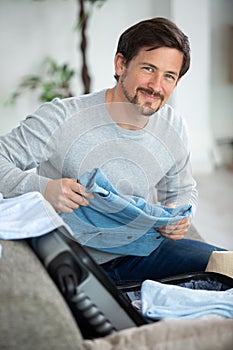 happy man on couch preparing travel back and packing suitcase