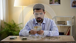 Happy man counting coins and dollar bills at home and smiling, budget savings