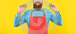 Happy man crop view in red apron holding fresh limes citrus fruits yellow background, fruiterer photo