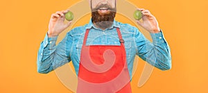 Happy man crop view in red apron holding fresh limes citrus fruits yellow background, fruiterer photo
