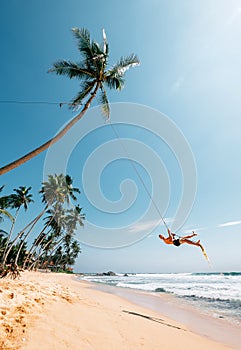 Happy man dangles on tropical palm tree swing