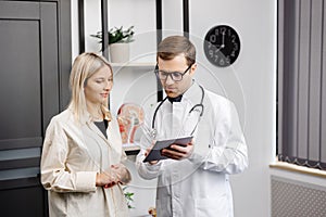 Happy man doctor showing tablet woman patient in clinic office interior. Health care, visit to family therapist, treatment of