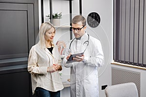 Happy man doctor showing tablet woman patient in clinic office interior. Health care, visit to family therapist, treatment of