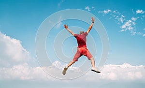 Happy man dressed red jumping over the clouds with Annapurna range mountains on background as he had trekking to Shanti Peace