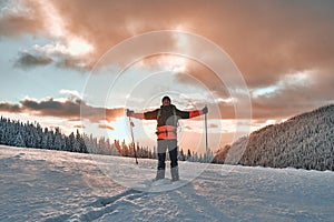 Happy man dressed in winter sports warm clothes with a tourist backpack and trekking poles in the snowy pine mountains. In the