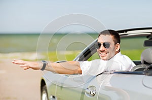 Happy man driving cabriolet car and waving hand