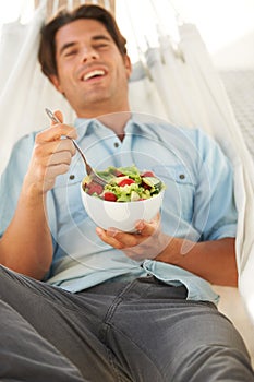 Happy, man and eating a healthy salad in a hammock for travel, freedom and wellness, diet or detox on vacation. Food