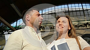 Happy Man Embracing Smiling Female While Situating On Escalator. Glad Lovers During Journey Concept. Spending Honeymoon