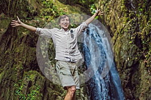 Happy man enjoying amazing tropical waterfall raised hands Travel Lifestyle and success concept vacations into the wild