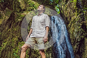 Happy man enjoying amazing tropical waterfall raised hands Travel Lifestyle and success concept vacations into the wild