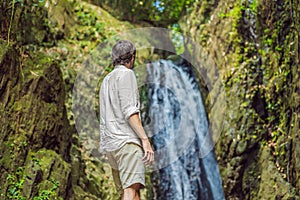 Happy man enjoying amazing tropical waterfall raised hands Travel Lifestyle and success concept vacations into the wild