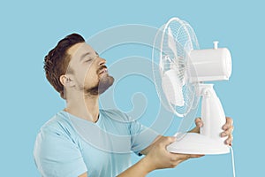 Happy man enjoying cool, fresh air blowing from an electric fan on a hot summer day