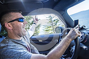 Happy man enjoying a road trip in his car on a sunny day