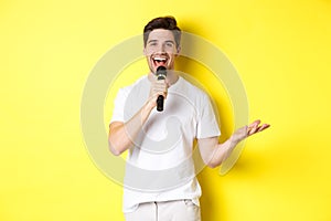 Happy man entertainer performing, talking in microphone, making speech or stand-up show, standing over yellow background