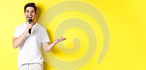 Happy man entertainer performing, talking in microphone, making speech or stand-up show, standing over yellow background