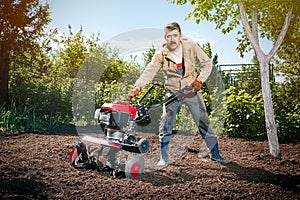 Happy man Farmer plows the land with a cultivator, preparing it