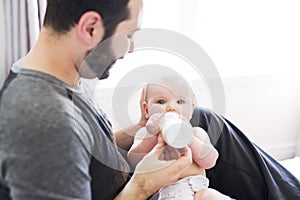 Happy man feeding milk to baby girl at home