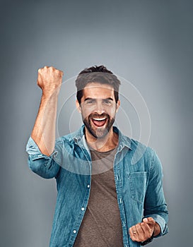 Happy man, fist and celebration for winning, success or victory against a grey studio background. Excited portrait of