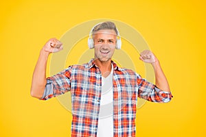 Happy man flex strong arms listening to music in modern headphones yellow background, sound power