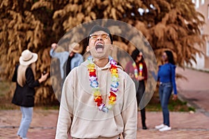 Happy man with flower necklace laughing while having a party with friends outdoors.