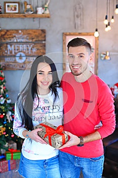 Happy man gifting woman present in decorated room, celebrating Christmas. photo