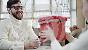 Happy man gives a big box full of flowers to his wife while sitting in a cafe