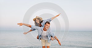 Happy man giving piggyback ride to his woman and laughing at tropical beach. Smiling guy in love carrying on back her