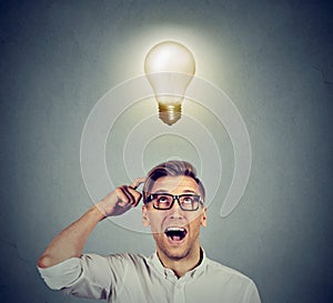 Happy man in glasses looking up at bright light idea bulb above head