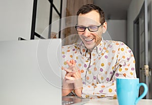 happy man in glasses using laptop, writing email or message, chatting, shopping, successful freelancer working online