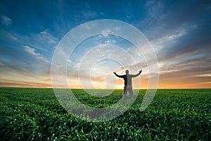 Happy man on green field of wheat at sunrise