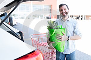 Happy Man With Grocery Bag Standing By Car