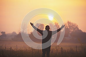 A happy man with hands in the air standing in the field at sunrise