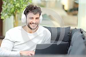 Happy man with headphone and laptop looks at you at home