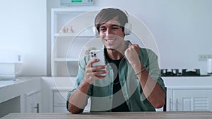 Happy man in headphones looking at smartphone celebrate success mobile win online bet. Lucky young male reading good