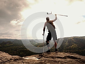 Happy man hiker holding medicine crutch above head, injured knee fixed in knee brace feature.