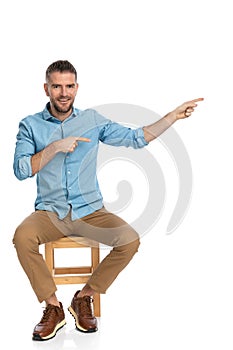 Happy man in his forties wearing denim shirt and pointing fingers to side