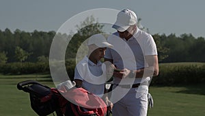 Happy man with his son golfers walking on perfect golf course at summer day